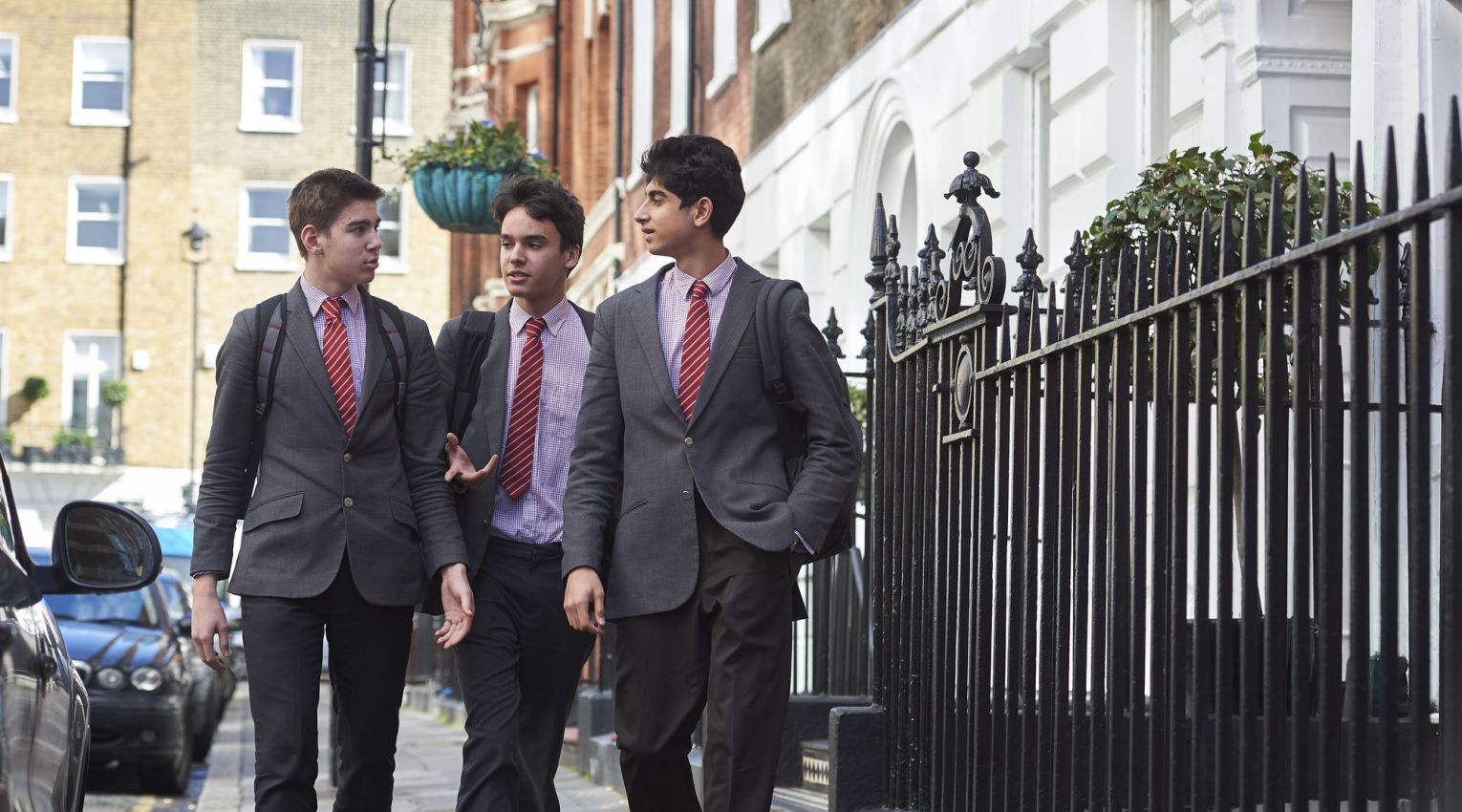 three teenage boys in suits walking along street